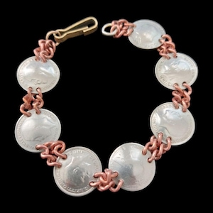 May include: A handcrafted bracelet made from silver coins and copper wire. The coins are linked together with copper wire and have a detailed design. The bracelet has a gold-coloured clasp. The design is vintage and unique.