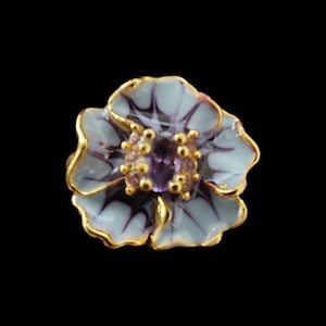 Könnte beinhalten: Ein blütenförmiger Ring mit einem goldfarbenen Band. Der Ring hat eine hellblaue und lila Blume mit goldenen Verzierungen. Das Zentrum der Blume hat eine Ansammlung kleiner rosa und lila Steine.