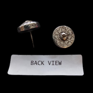 May include: Silver stud earrings with a decorative design. One earring is shown from the side, revealing a post and a detailed edge. The other earring shows the back, with a pattern of small hearts. The text "BACK VIEW" is visible.
