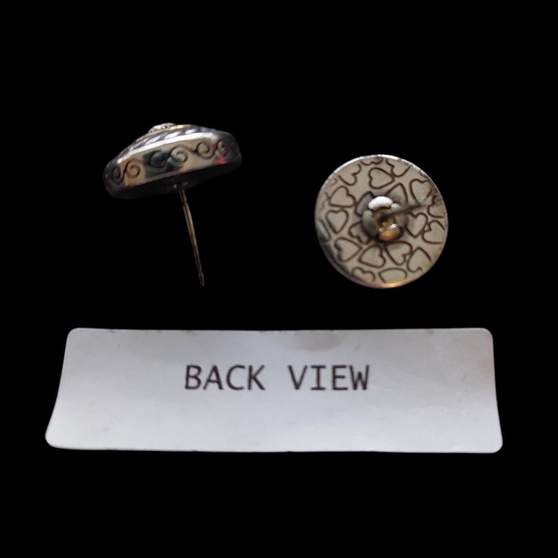 May include: Silver stud earrings with a decorative design. One earring is shown from the side, revealing a post and a detailed edge. The other earring shows the back, with a pattern of small hearts. The text "BACK VIEW" is visible.
