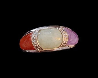 May include: A silver ring with a rectangular pale green center stone, flanked by a red stone on one side and a lavender stone on the other. The ring has a decorative gold band with small clear stones.