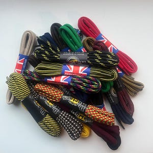 Può includere: Una collezione di lacci colorati, con design a tinta unita e fantasia. I lacci sono disponibili in vari colori, come rosso, verde, giallo e nero. Alcuni sono confezionati con etichette con la bandiera britannica e la scritta "Made in England".