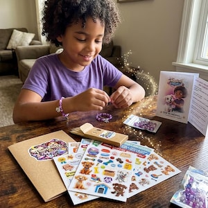 May include: A child is making a purple beaded bracelet with a charm. The table has a craft kit with stickers, beads, and a booklet titled "Magical Mutts". The stickers feature cartoon dogs and dog-related items. The kit is designed for making jewelry.