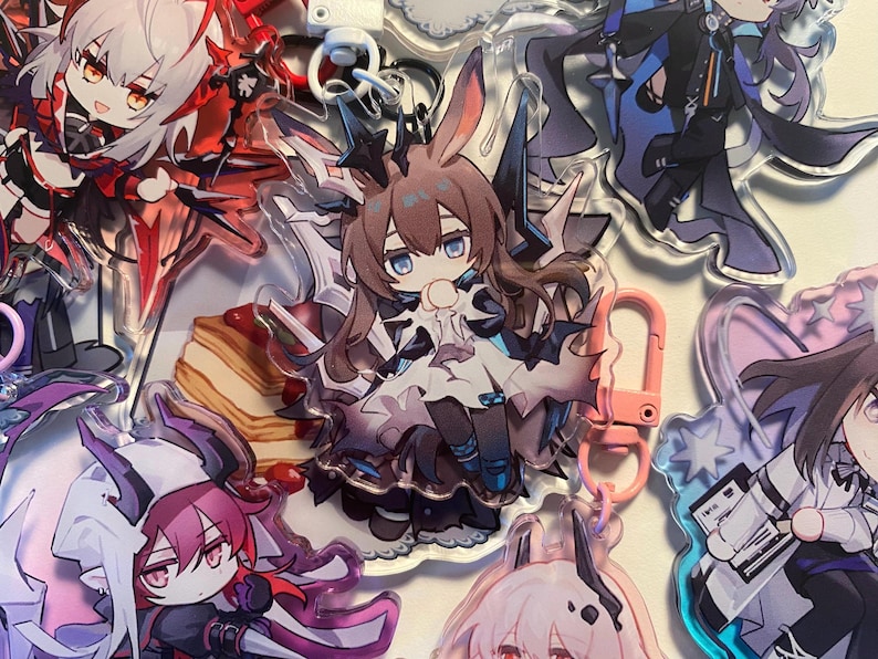 May include: A collection of anime-style acrylic keychains featuring various characters. The keychains showcase detailed artwork with vibrant colors, including characters with bunny ears, and other fantasy elements. Some keychains have pink or silver clasps.