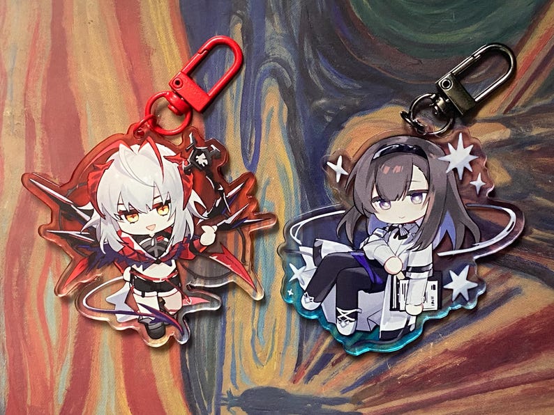 May include: Two anime-style acrylic keychains. One features a character with white hair and red accents, the other a character with dark hair and a white and black outfit. Both have metal clasps for attaching to keys or bags.