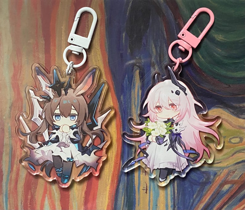 May include: Two anime-style acrylic keychains. One features a brown-haired character with blue accents and a white clip. The other has a pink-haired character with a pink clip. Both have detailed character designs and are attached to metal clasps.