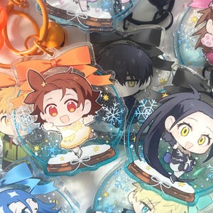 May include: A collection of anime-style character keychains. Each keychain features a colorful cartoon character inside a clear, snow globe-shaped acrylic charm. The charms are adorned with snowflakes and glitter, and some have decorative bows.