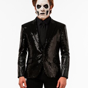 May include: A black sequin blazer with leather sleeves, worn with a black shirt and tie. The person in the image has white face paint with black accents. The blazer has a classic notched lapel and two front pockets.