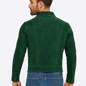 May include: A dark green suede jacket with a classic collar and buttoned cuffs. The jacket has a tailored fit and is worn with blue jeans. The back view of the jacket shows the seams and design details.