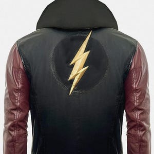 Puede incluir: Chaqueta de cuero negra con mangas burdeos y cuello negro. La espalda presenta un rayo dorado dentro de un círculo negro. La chaqueta tiene dobladillo y puños acanalados, ofreciendo un estilo bomber clásico.