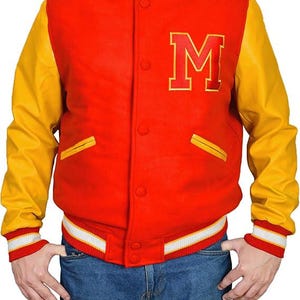 May include: A red and yellow varsity jacket with the letter "M" on the chest. The jacket has yellow sleeves, a red body, and white and red striped cuffs and waistband. The jacket is buttoned up and has two front pockets.