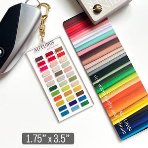 May include: A clear acrylic keychain with a gold clasp, featuring a color palette labeled "AUTUMN Colors To Go." The palette includes various shades of red, pink, beige, green, yellow, and blue. The keychain measures 1.75" x 3.5".