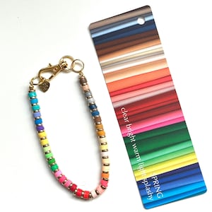 May include: A colorful beaded bracelet with gold-tone accents and a lobster clasp. The bracelet features a rainbow of colors, including red, pink, yellow, and blue. A color palette card with the text "clear bright warm light splashy SPRING" is next to the bracelet.