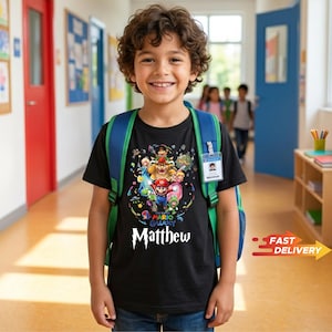 May include: A black short-sleeved t-shirt featuring a colorful Super Mario Galaxy graphic print with various characters including Mario, Bowser, and Princess Peach. The text "The Super Mario Galaxy" and the name "Matthew" are printed in white.