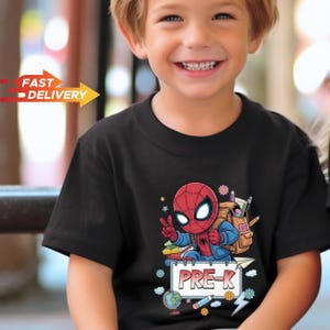 May include: A black short-sleeved t-shirt featuring a graphic of a cartoon Spider-Man character wearing a backpack, making a peace sign, and standing above a notepad with the text PRE-K, surrounded by school supplies like a globe and pencils.