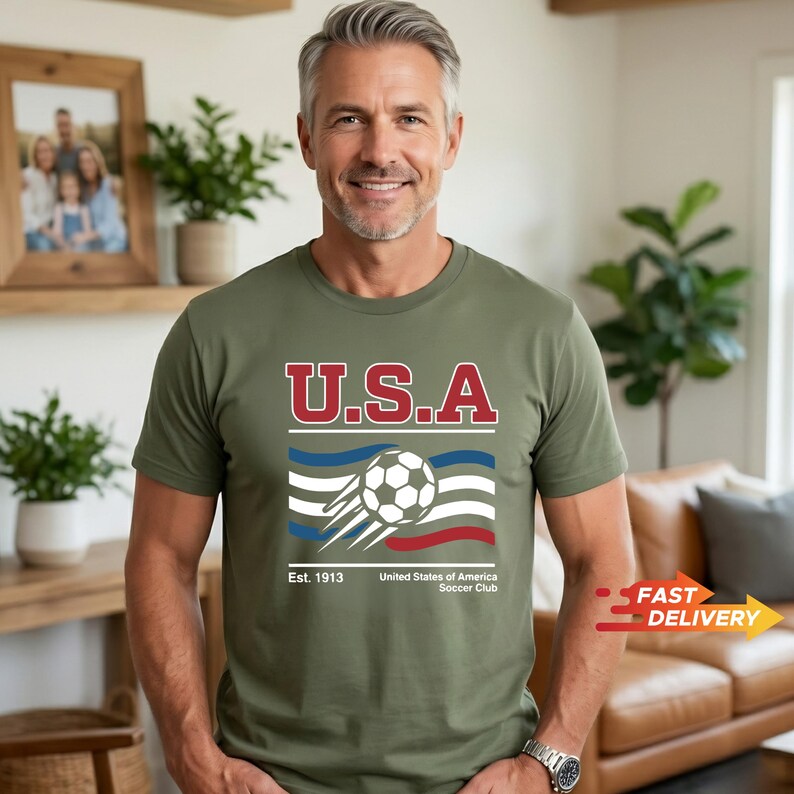 May include: Olive green t-shirt with the text "U.S.A" in red and white. Below the text is a soccer ball graphic with blue and red stripes. The shirt also includes the text "Est. 1913 United States of America Soccer Club."