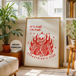 Może przedstawiać: Oprawiony wydruk z czerwoną ilustracją szkieletu pokazującego kciuk w górę, otoczony płomieniami. Tekst brzmi "It's Fine, I'm Fine, Everything's Fine." Grafika jest prezentowana w jasnym pomieszczeniu z roślinami.