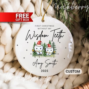 May include: A white ceramic Christmas ornament with gold string. The ornament features two cartoon teeth wearing Santa hats, with the text "First Christmas Without My Wisdom Teeth" and a name and year.