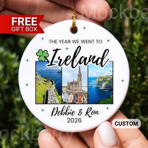 May include: A round white ceramic ornament featuring the text THE YEAR WE WENT TO Ireland, a green shamrock icon, and three rectangular photo panels showing Irish landscapes and architecture. The names Debbie & Ron and the year 2026 are printed below.