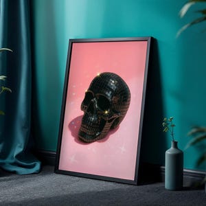 May include: Black framed art print featuring a disco ball skull on a pink background with sparkling accents. The skull is made of reflective, mirrored tiles. The artwork is leaning against a teal wall.