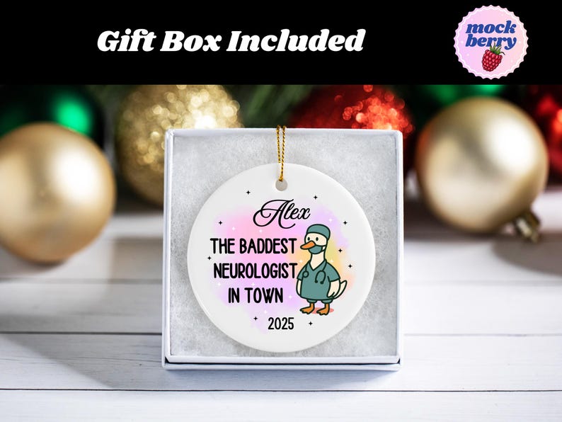 Puede incluir: Adorno de cer&aacute;mica blanca en una caja de regalo. El adorno presenta un pato de dibujos animados con uniforme m&eacute;dico, con el texto "Alex, The Baddest Neurologist in Town, 2025". El fondo tiene un efecto acuarela con tonos rosas y amarillos. Se adjunta un cord&oacute;n dorado para colgar.