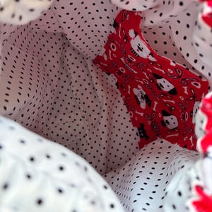 Peut inclure: Un sac &agrave; cordon dot&eacute; d'une doublure int&eacute;rieure blanche &agrave; pois noirs et d'une poche int&eacute;rieure rouge orn&eacute;e d'un motif r&eacute;p&eacute;titif de t&ecirc;tes de chiens blanches et noires, d'os et de fleurs, avec une fermeture &agrave; cordon de couleur rouge.