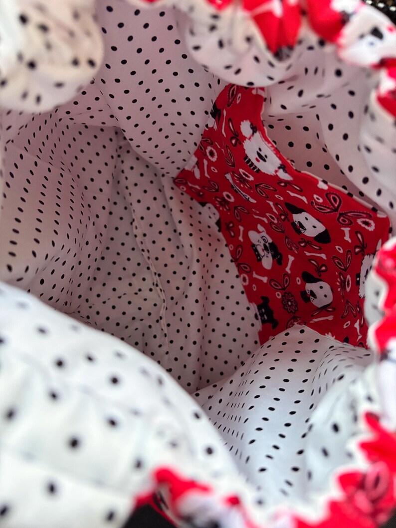 Peut inclure: Un sac &agrave; cordon dot&eacute; d'une doublure int&eacute;rieure blanche &agrave; pois noirs et d'une poche int&eacute;rieure rouge orn&eacute;e d'un motif r&eacute;p&eacute;titif de t&ecirc;tes de chiens blanches et noires, d'os et de fleurs, avec une fermeture &agrave; cordon de couleur rouge.