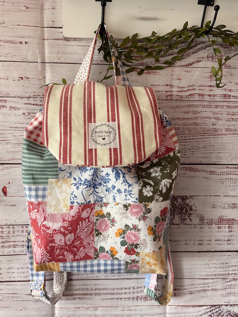 Peut inclure: Un sac &agrave; dos en patchwork compos&eacute; de divers motifs floraux, vichy et ray&eacute;s dans des tons de rouge, bleu, vert et jaune. Le rabat sup&eacute;rieur pr&eacute;sente des rayures verticales rouges et blanches avec une &eacute;tiquette blanche indiquant Pretti Bags Made in USA.