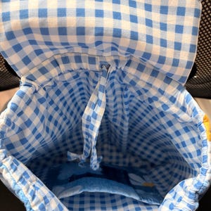 Peut inclure: Un sac &agrave; dos en tissu arborant un motif &agrave; carreaux vichy bleu clair et blanc. L'int&eacute;rieur comprend un syst&egrave;me de fermeture &agrave; cordon coulissant et une poche ouverte unique sur le panneau arri&egrave;re. Le rabat sup&eacute;rieur est doubl&eacute; du m&ecirc;me tissu vichy.