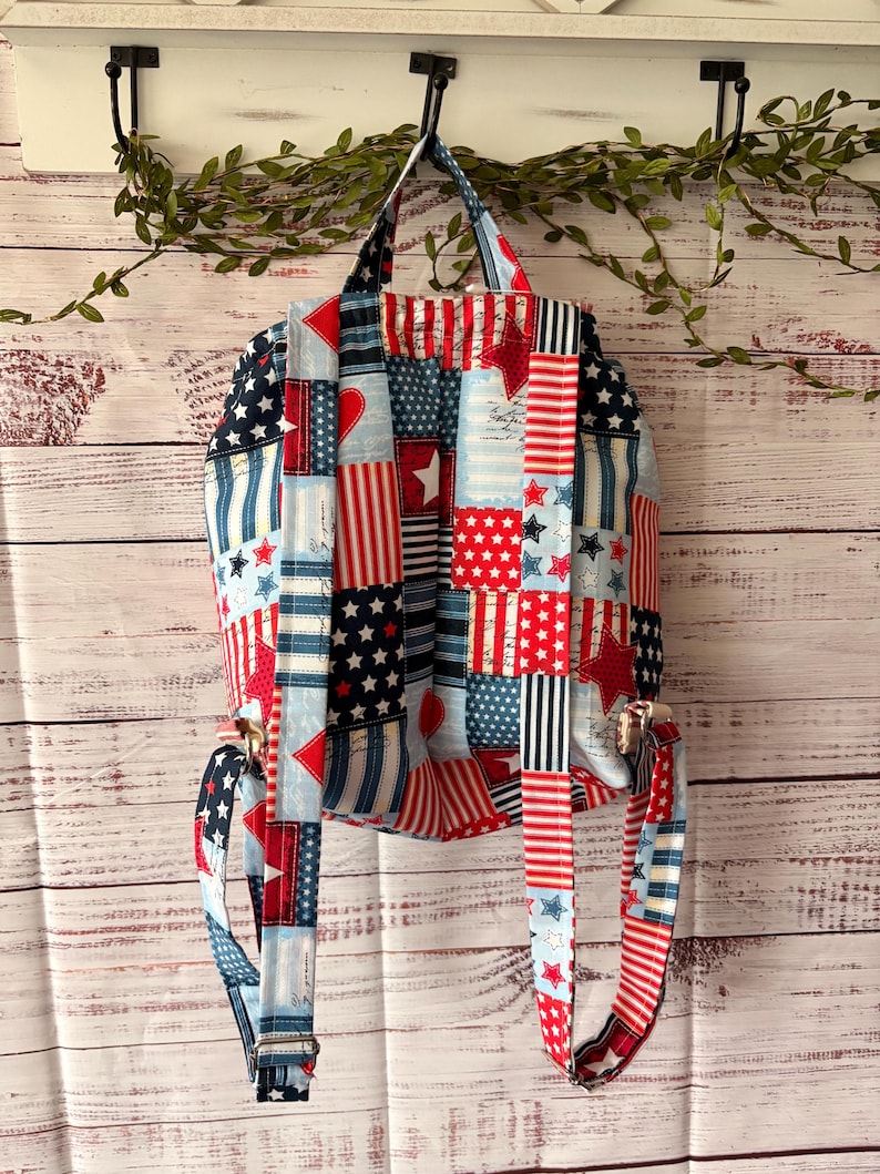 Peut inclure: Un sac &agrave; dos en tissu avec un motif patchwork aux couleurs rouge, blanc et bleu. Le design comprend des &eacute;toiles, des rayures et des c&oelig;urs. Il poss&egrave;de deux bretelles r&eacute;glables et une poign&eacute;e sup&eacute;rieure, fabriqu&eacute;s dans le m&ecirc;me tissu &agrave; motifs.