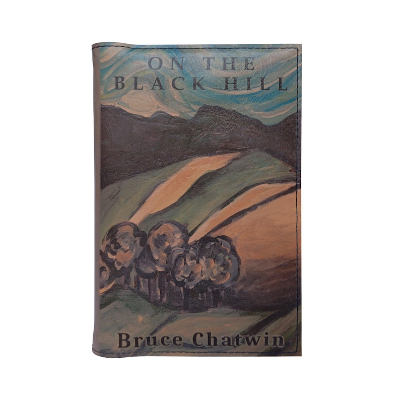 May include: A book cover with a painted landscape scene of a green hill with a brown path leading up to a dark blue mountain range. The title "On the Black Hill" is printed in black text on the cover. The author's name, "Bruce Chatwin", is printed in black text at the bottom of the cover.