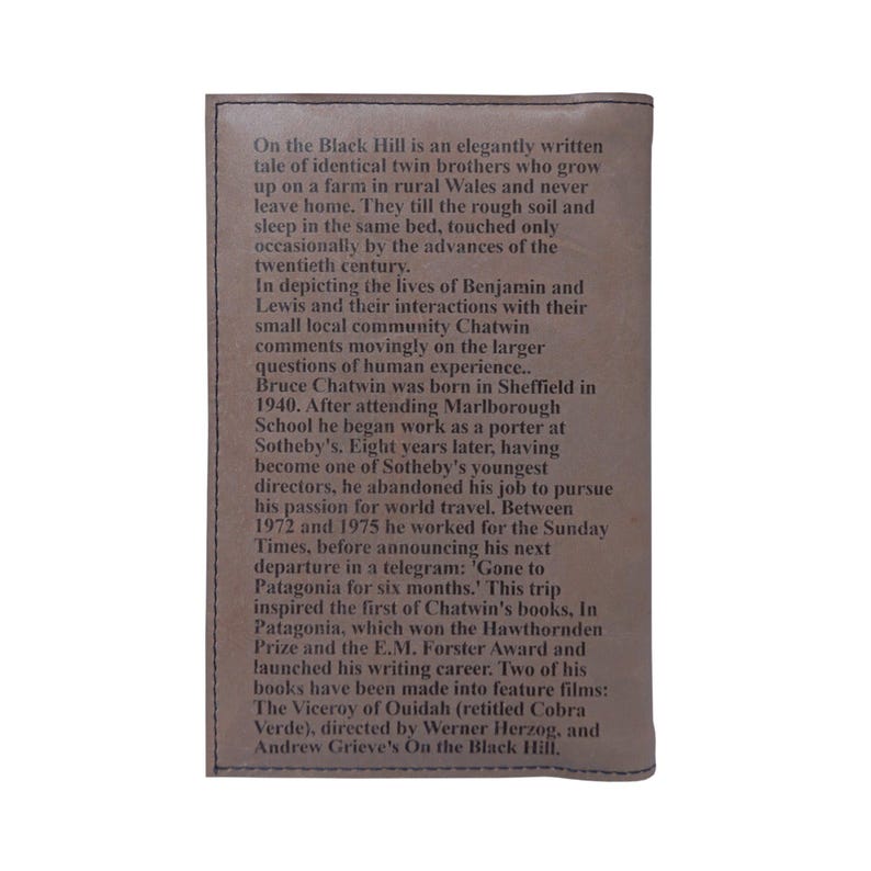 May include: A brown leather-bound book with the title "On the Black Hill" embossed on the front cover. The text describes the lives of twin brothers who grow up on a farm in rural Wales and never leave home. The book was inspired by the author's travels to Patagonia.