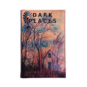 Puede incluir: Una portada de libro con el t&iacute;tulo "DARK PLACES" y el nombre de la autora, Gillian Flynn. La portada presenta una pintura a la acuarela de una escena rural con un molino de viento, una casa y &aacute;rboles desnudos.