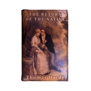Op de afbeelding: Een vintage boekomslag met een bruine lederachtige textuur. De omslag toont een schilderij van een stel dat op een stenen bank zit. De titel "THE RETURN OF THE NATIVE" en de auteur "Thomas Hardy" zijn gedrukt in gouden letters.