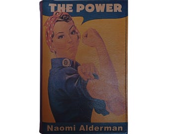 Könnte beinhalten: Eine Ledergeldbörse mit einer Illustration im Vintage-Stil einer Frau, die ihren Arm beugt, mit dem Text "THE POWER" in einer Sprechblase. Der Name "Naomi Alderman" ist unten aufgedruckt. Die Geldbörse hat einen blauen Rand.
