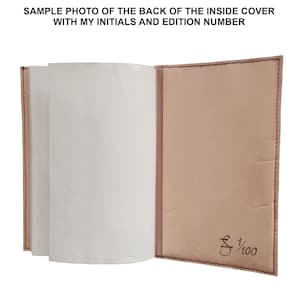 Puede incluir: Diario de cuero abierto con p&aacute;ginas blancas en blanco. La cubierta interior es de color marr&oacute;n claro con costuras marrones oscuras. El texto "SAMPLE PHOTO OF THE BACK OF THE INSIDE COVER WITH MY INITIALS AND EDITION NUMBER" est&aacute; en la parte superior. Iniciales y n&uacute;mero de edici&oacute;n impresos.