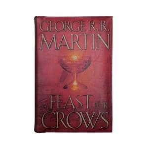 May include: A Feast for Crows by George R.R. Martin book cover with a red background and a golden goblet with a glowing light inside. The title is in a gold font.