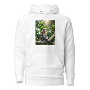 Puede incluir: Sudadera con capucha blanca con una imagen de un mono sentado en una rama de árbol en un bosque verde. El mono es de color marrón claro. El fondo muestra un follaje denso y luz solar.