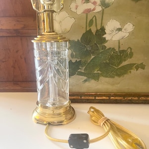 May include: A table lamp featuring a clear, vertically fluted glass body with a decorative fan-like pattern. The lamp has a polished brass base and top fixture, a gold-toned electrical cord, and a black inline switch with a two-prong plug.