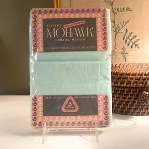 May include: A vintage package of Mohawk Famous Muslin pillowcases. The packaging is light blue with a brown and pink label that reads "Stevens Mohawk Famous Muslin". The text "The Thrift Pillow Case of the Nation" is also visible.