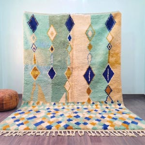 May include: A large rectangular area rug featuring a soft pile with a geometric pattern of diamonds in shades of mint green, cream, mustard yellow, and deep blue. The bottom border displays a dense diamond grid with a cream-colored fringe edge.