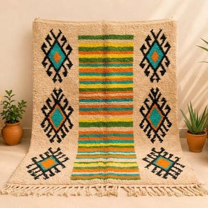 May include: A rectangular beige area rug featuring a central vertical panel of horizontal stripes in green, yellow, and orange. The rug is decorated with six symmetrical black diamond-shaped geometric motifs with teal and orange centers and fringe.