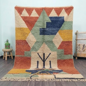 May include: A rectangular area rug featuring a high-pile texture and a geometric pattern in shades of terracotta, mustard yellow, sage green, navy blue, and cream. The design includes triangular and stepped motifs with a central dark blue symbol.