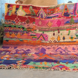 May include: A large rectangular area rug featuring a vibrant, multi-colored geometric pattern with horizontal bands of pink, orange, blue, green, and cream. The rug has a thick, textured pile and a fringed edge along the bottom border.