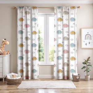 May include: White window curtains with a repeating pattern of colorful cartoon fish and small white clouds. The fish are in shades of yellow, pink, blue, and gray, outlined in black. The curtains are hanging in front of a window.
