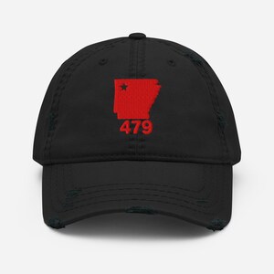 Puede incluir: Gorra de béisbol negra desgastada con un diseño rojo bordado del contorno del estado de Arkansas, una estrella y el número "479". La gorra tiene una visera curva y un aspecto vintage desgastado.
