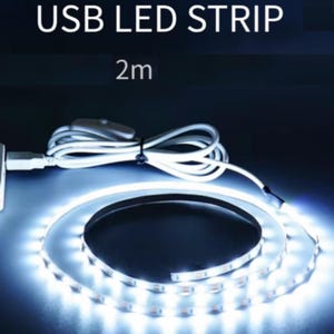 K&ouml;nnte beinhalten: 2 Meter USB-LED-Streifen, aufgerollt und emittiert hellwei&szlig;es Licht. Der flexible Streifen hat einen USB-Anschluss und ein wei&szlig;es Netzkabel mit einem Inline-Schalter. Der Text "USB LED STRIP" und "2m" sind oben abgebildet.