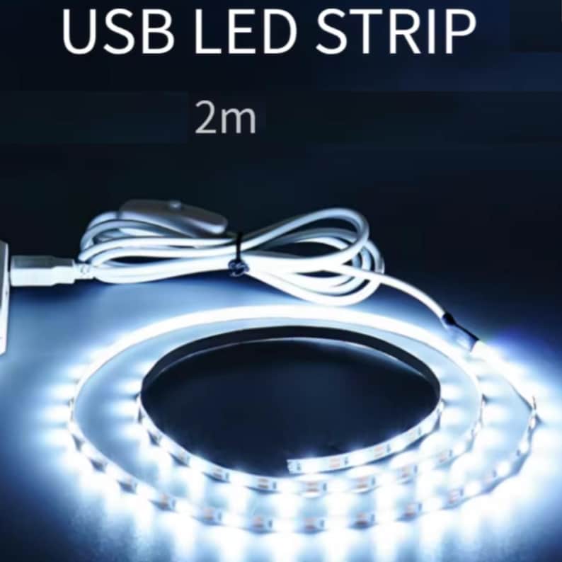 K&ouml;nnte beinhalten: 2 Meter USB-LED-Streifen, aufgerollt und emittiert hellwei&szlig;es Licht. Der flexible Streifen hat einen USB-Anschluss und ein wei&szlig;es Netzkabel mit einem Inline-Schalter. Der Text "USB LED STRIP" und "2m" sind oben abgebildet.