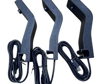 May include: Three black, textured, curved stands with attached black USB cables. Each stand has a curved arm and a base with a clip. The cables are neatly bundled. The stands are designed for electronic devices.