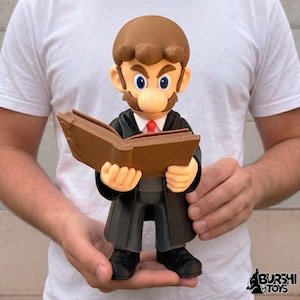 Puede incluir: Figura de un personaje con bigote, pelo y cejas marrones, que lleva una túnica negra y sostiene un libro marrón. El personaje tiene ojos azules, una corbata roja y una nariz bronceada. Juguete de colección.